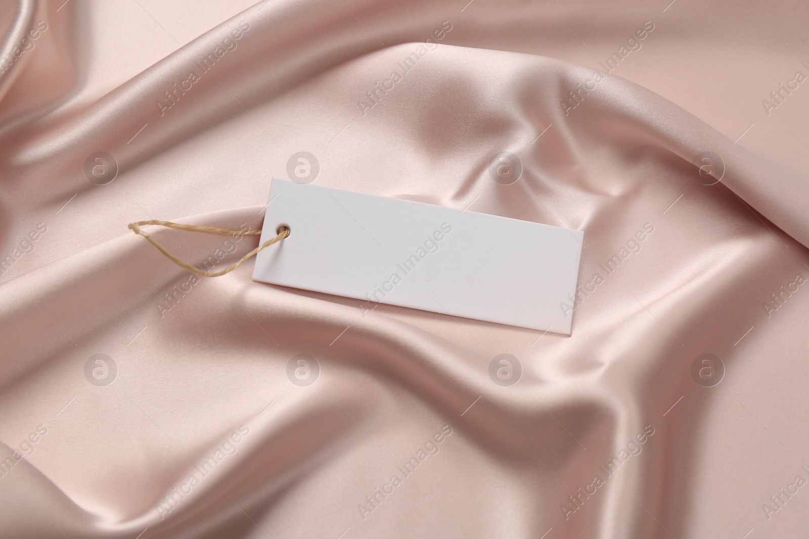 Photo of Blank white tag on pink silky fabric. Space or text