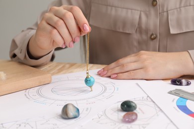 Photo of Astrologer using natal chart and pendulum for making forecast of fate at table, closeup. Fortune telling