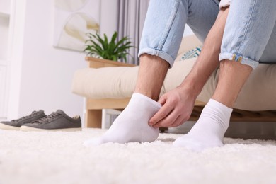 Photo of Man putting on white socks at home, closeup. Space for text
