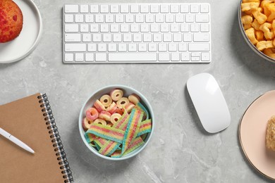 Photo of Bad eating habits at workplace. White keyboard, mouse and different snacks on grey marble table, flat lay