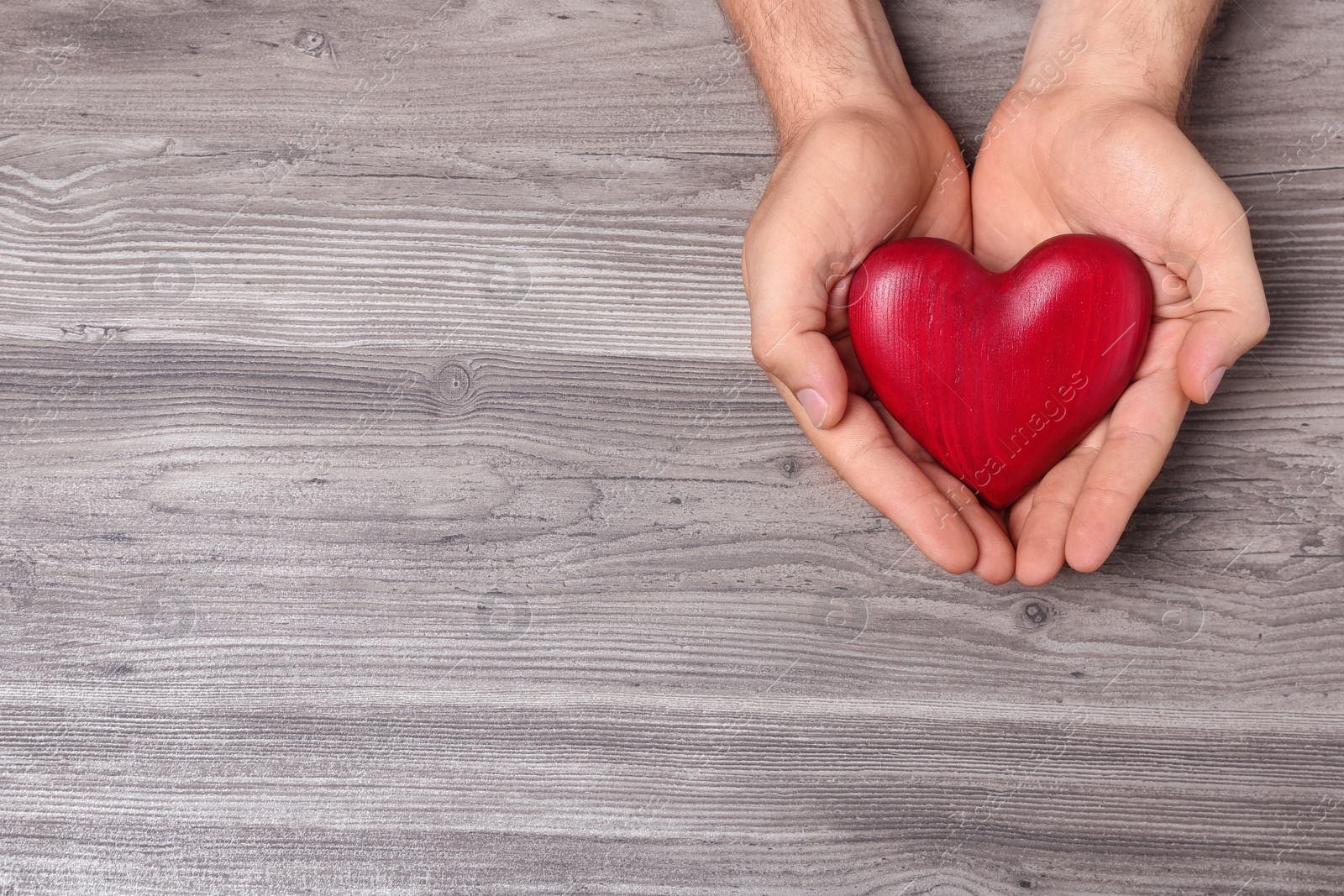 Photo of Young man holding red heart on grey wooden background, top view with space for text. Donation concept