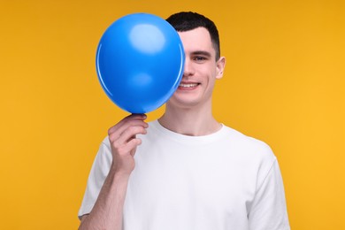 Photo of Happy young man with light blue balloon on yellow background