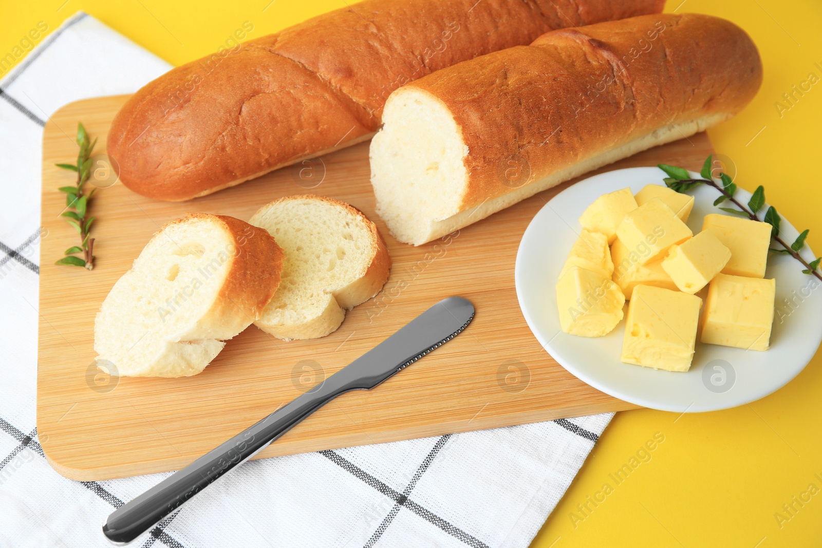 Photo of Whole and cut baguettes with fresh butter on yellow background