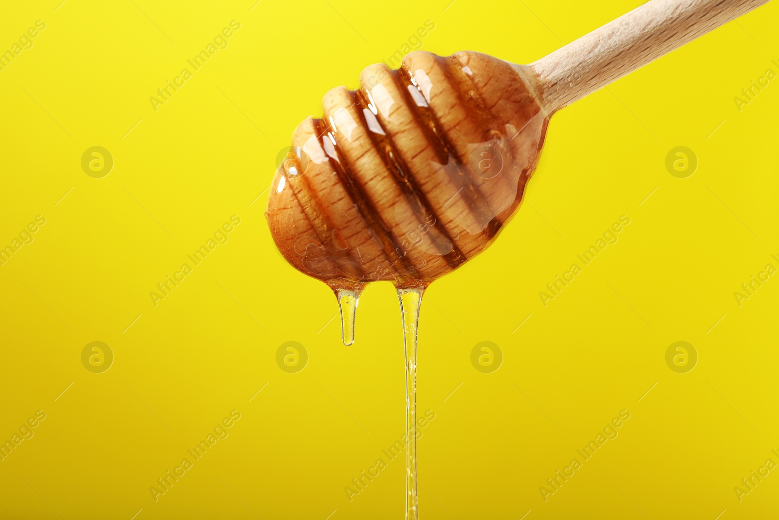 Photo of Delicious honey flowing down from dipper against yellow background, closeup