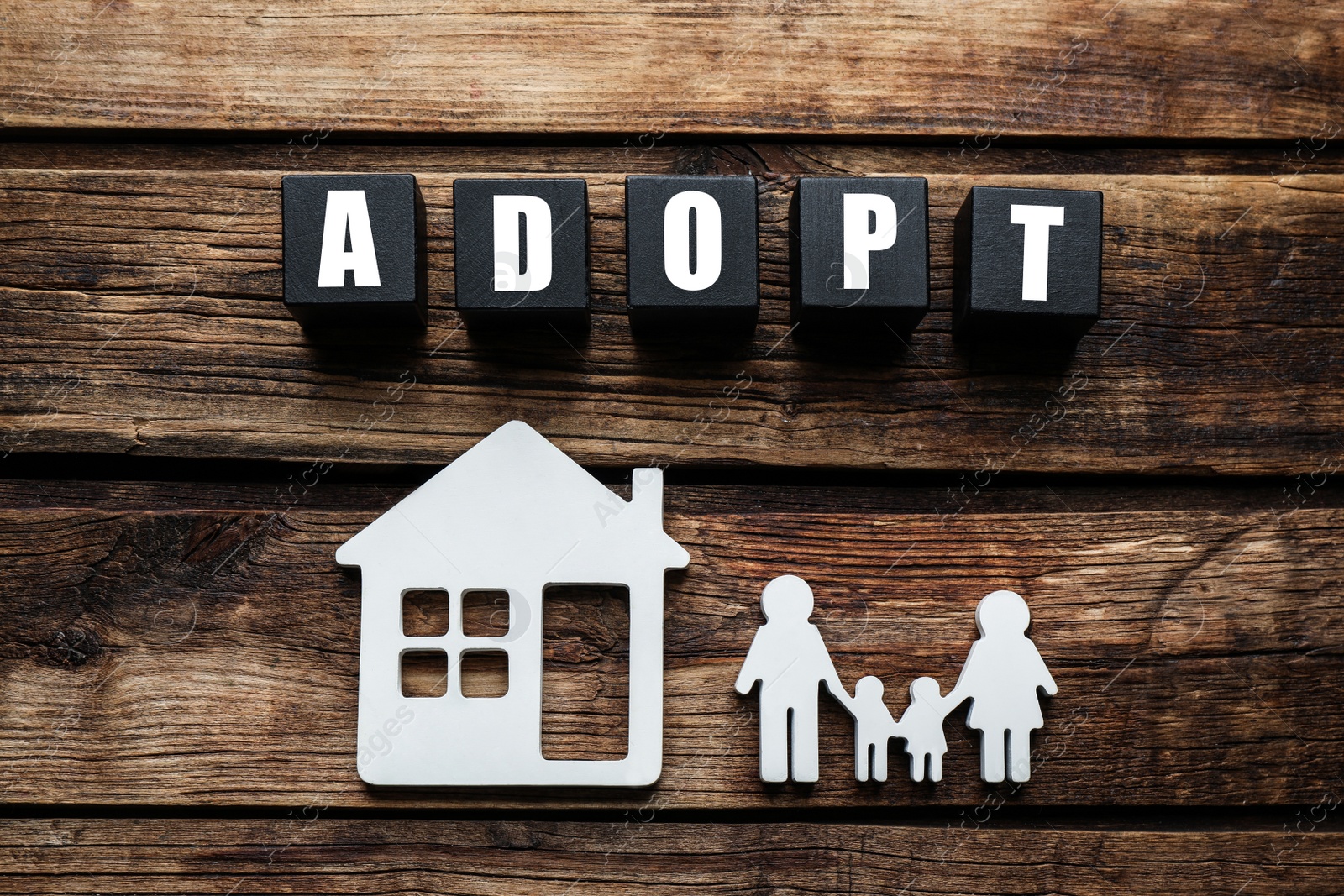 Photo of Family figure, house and word Adopt made of cubes on wooden table, flat lay