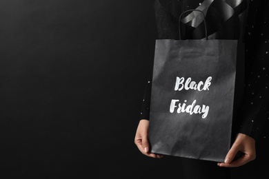 Photo of Woman holding shopping bag with words Black Friday on dark background, closeup. Space for text