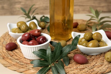 Photo of Bottle of oil, olives and tree twigs on table