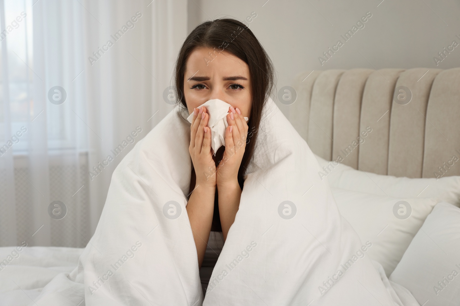 Photo of Sick young woman with tissue wrapped in blanket at home