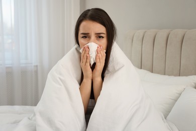 Sick young woman with tissue wrapped in blanket at home