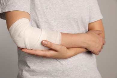 Photo of Woman with arm wrapped in medical bandage on light grey background, closeup