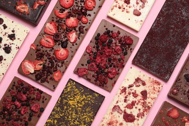 Different chocolate bars with freeze dried fruits on pink background, flat lay