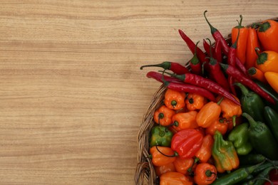 Photo of Wicker basket with many different fresh chilli peppers on wooden table, top view. Space for text