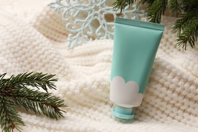 Photo of Winter skin care. Hand cream and fir branches on white knitted cloth