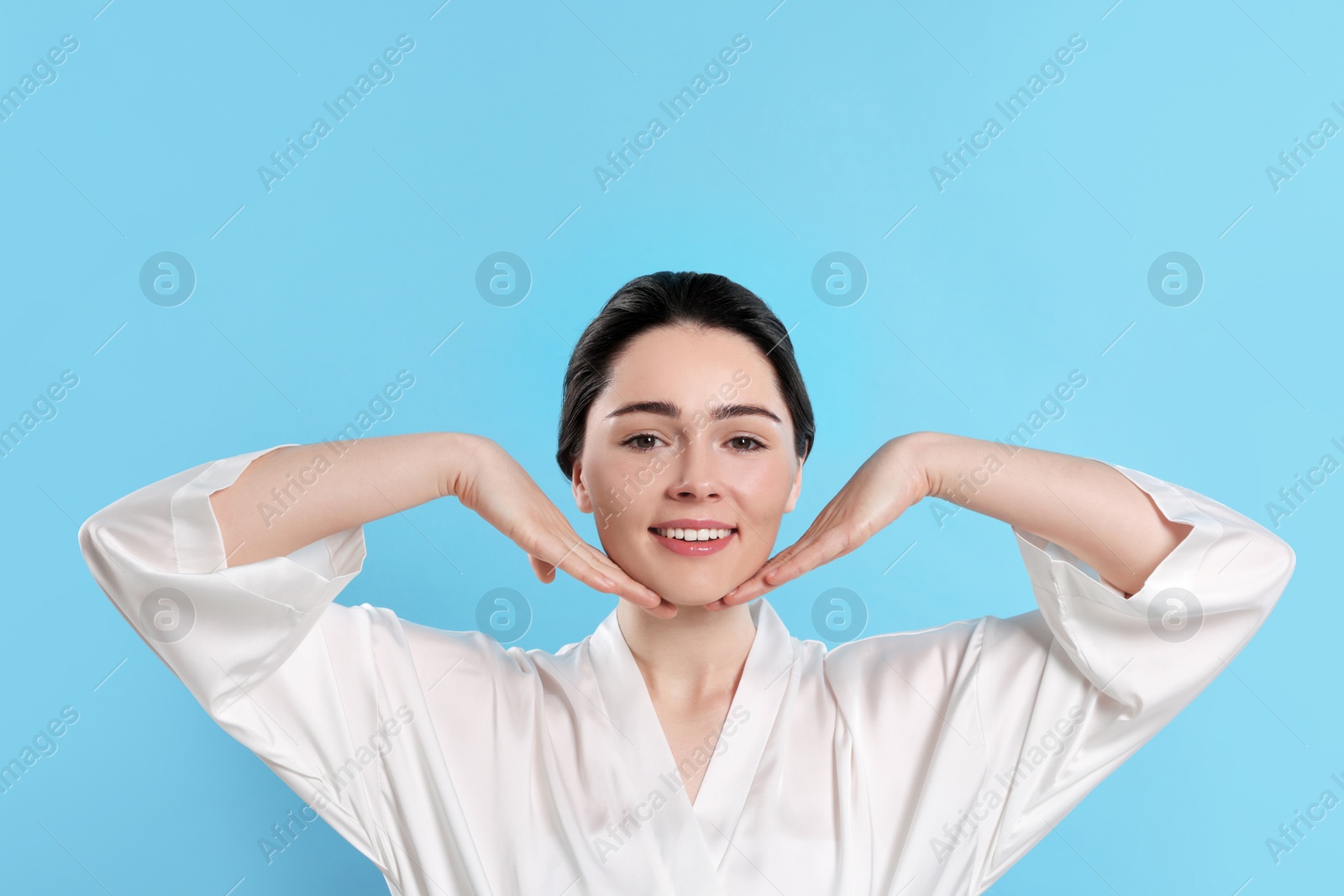 Photo of Young woman massaging her face on turquoise background