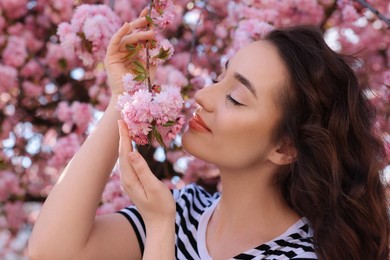 Beautiful woman smelling blossoming sakura tree on spring day