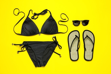 Photo of Flat lay composition with black swimsuit and beach accessories on yellow background