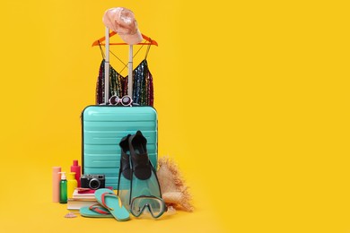 Photo of Suitcase, clothes and beach accessories on yellow background, space for text. Summer vacation