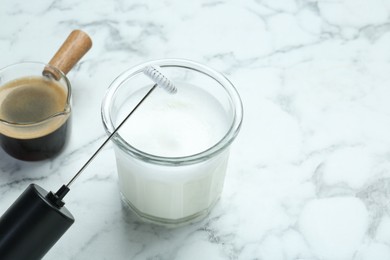 Photo of Mini mixer (milk frother), whipped milk in glass and coffee on white marble table, closeup. Space for text