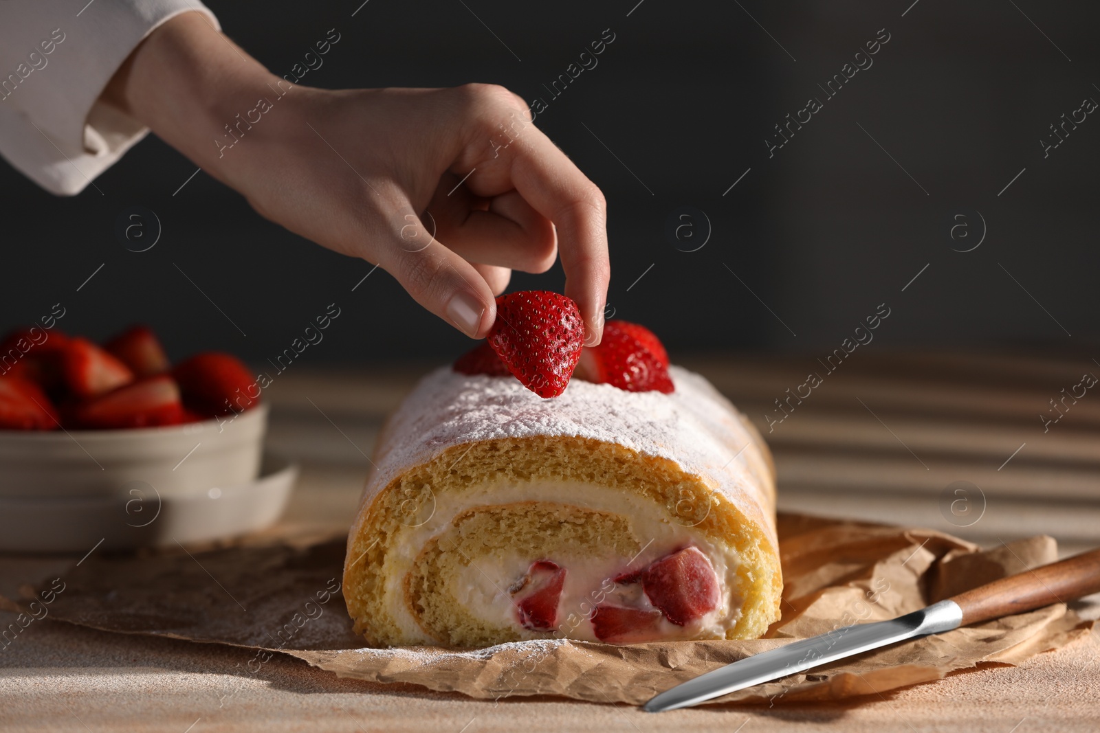 Photo of Woman decorating delicious cake roll with strawberries at table, closeup