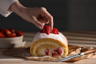 Photo of Woman decorating delicious cake roll with strawberries at table, closeup