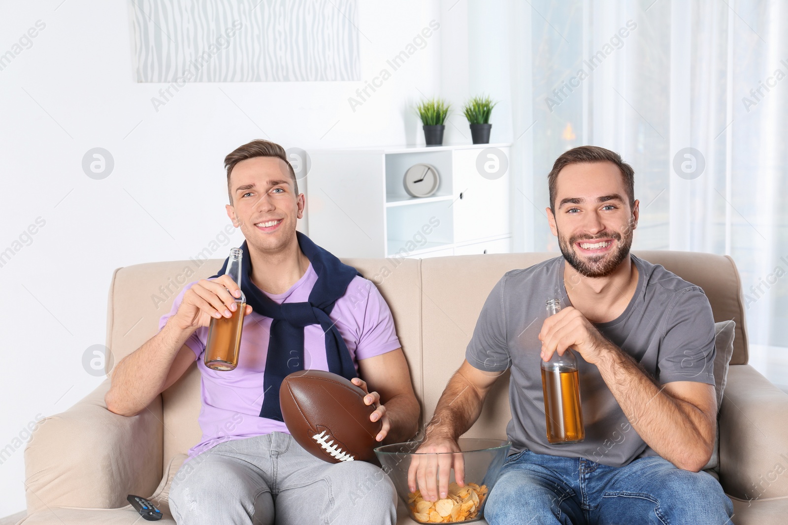 Photo of Young friends watching TV on sofa at home. Sport channel