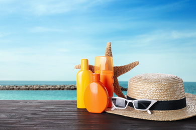 Image of Set of sun protection products and stylish accessories on wooden table near sea