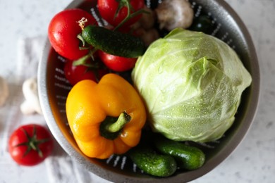 Metal colander with different wet vegetables on white textured table, top view