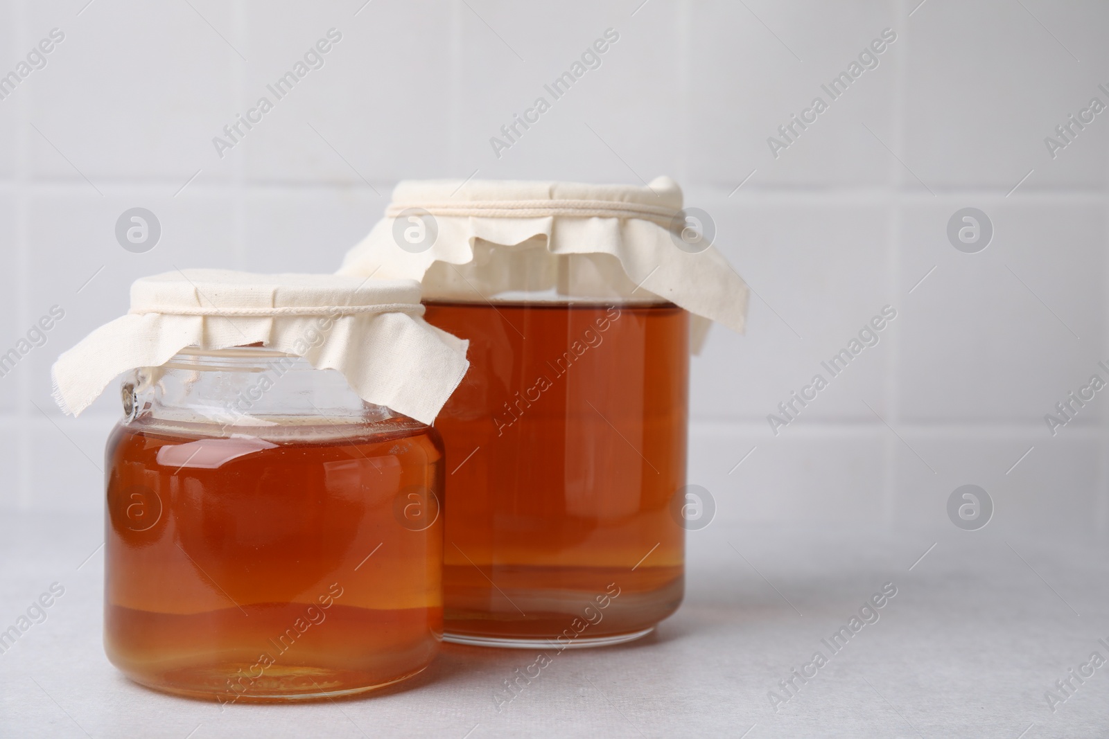 Photo of Tasty kombucha in glass jars on white table, space for text