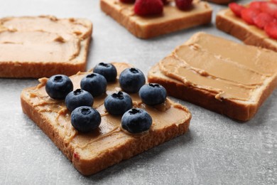 Photo of Tasty peanut butter sandwiches with fresh blueberries on gray table, closeup