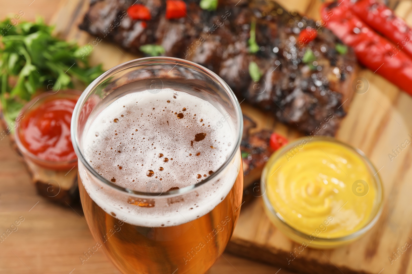 Photo of Glass of beer, tasty grilled ribs and sauces on table, closeup. Space for text