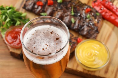 Glass of beer, tasty grilled ribs and sauces on table, closeup. Space for text