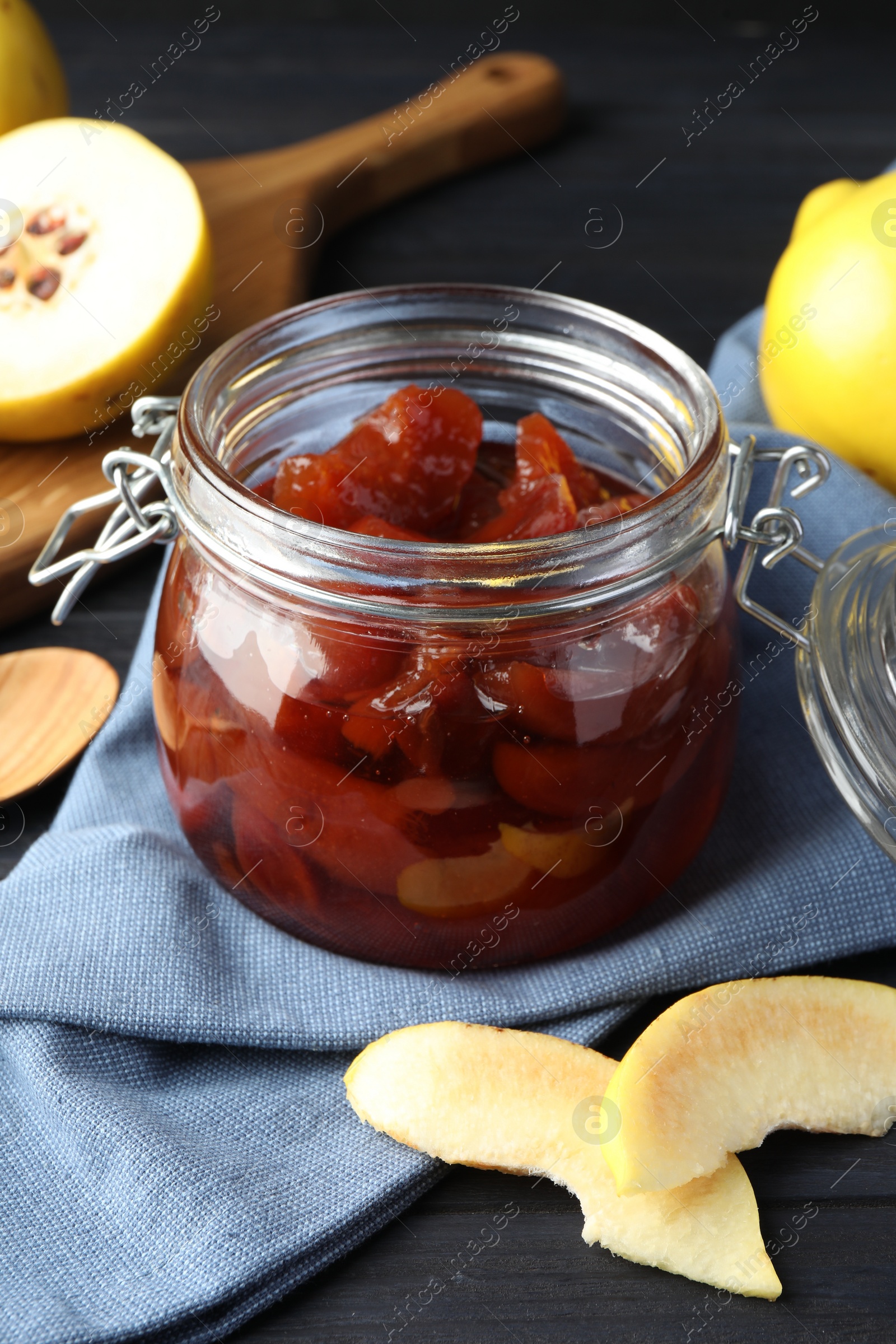 Photo of Quince jam in glass jar and fresh raw fruits on grey table, closeup