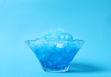 Shaving ice in glass dessert bowl on light blue background, closeup