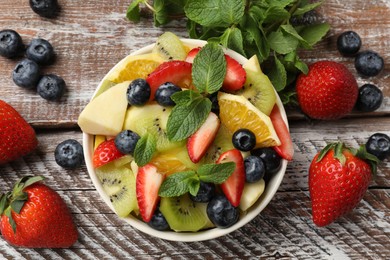 Photo of Tasty fruit salad in bowl and ingredients on wooden table, flat lay