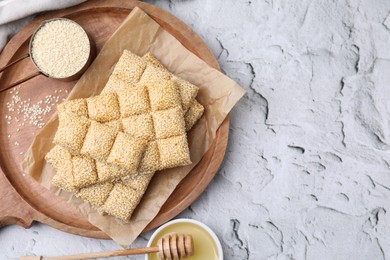 Photo of Wooden tray with delicious sweet kozinaki bars, sesame seeds and honey on white textured table, flat lay. Space for text