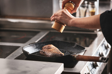 Photo of Female chef cooking meat on stove in restaurant kitchen, closeup