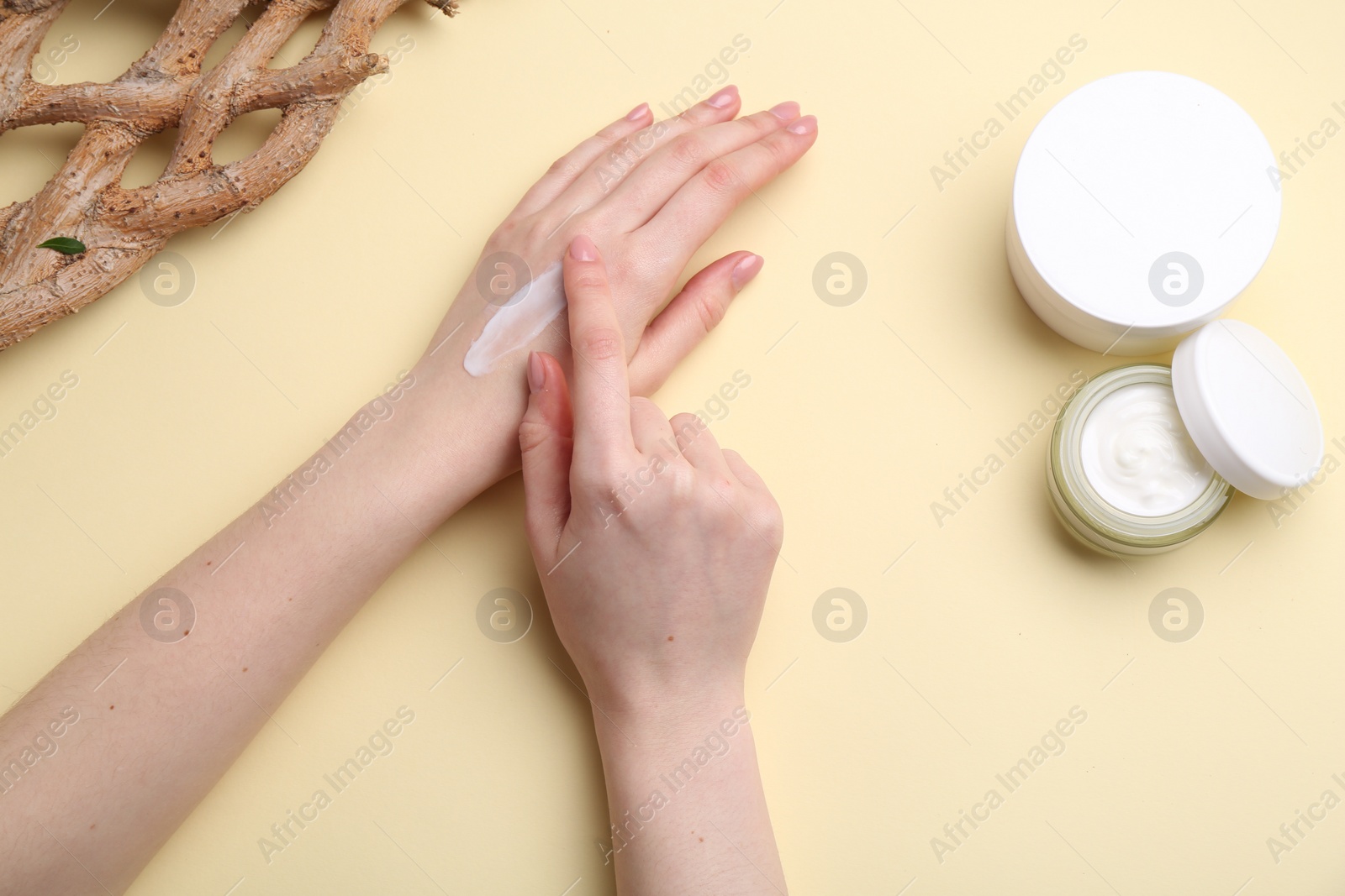 Photo of Woman applying hand cream on beige background, top view