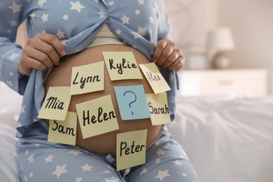 Photo of Pregnant woman with different baby names on belly in bedroom, closeup