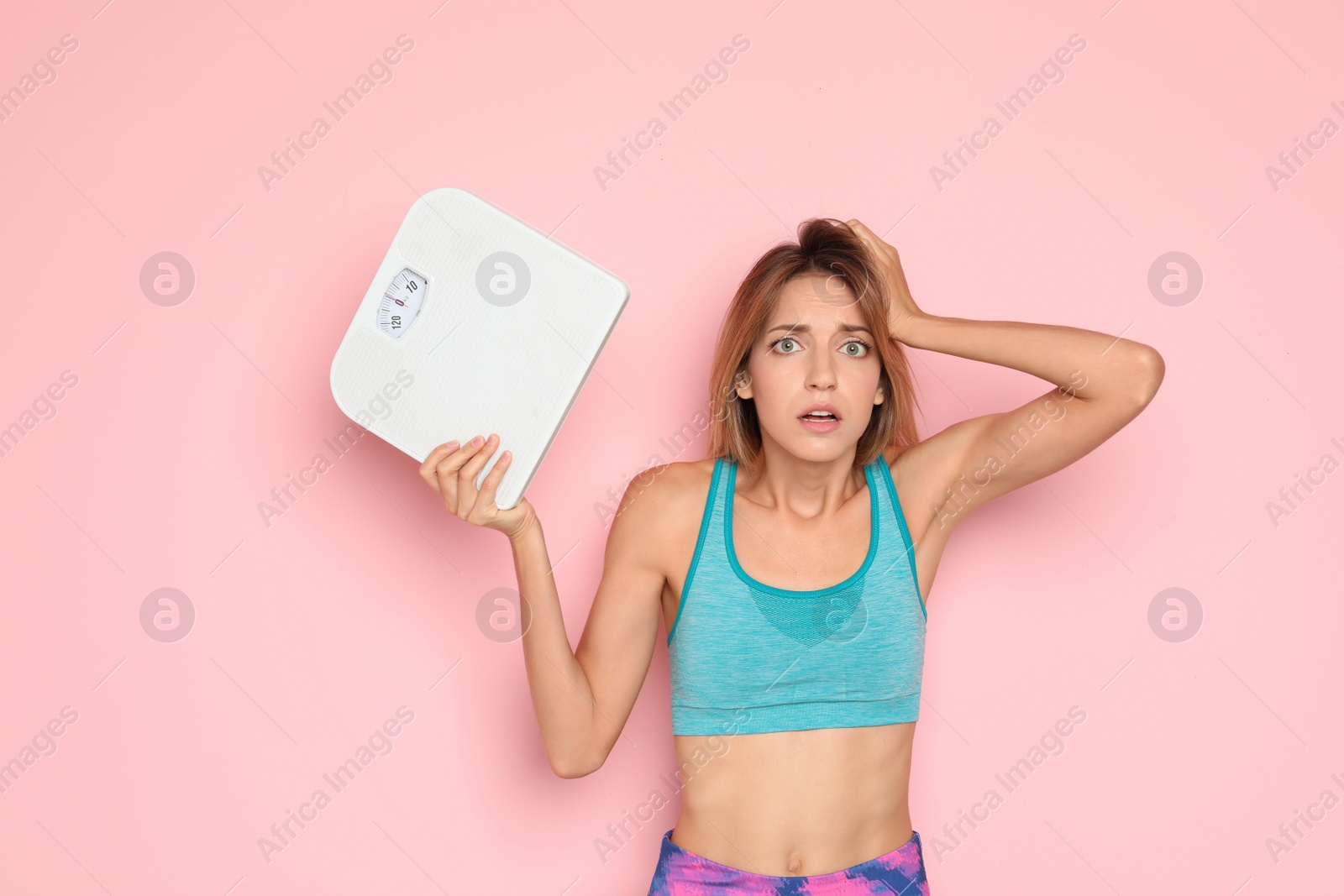 Photo of Worried young woman holding bathroom scales on color background. Weight loss diet