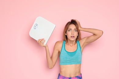 Photo of Worried young woman holding bathroom scales on color background. Weight loss diet