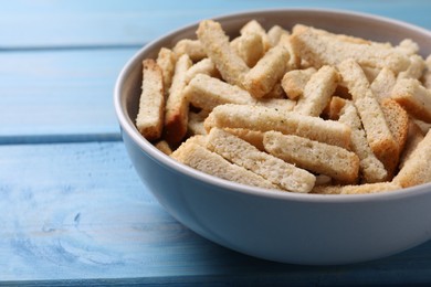 Photo of Crispy wheat rusks in bowl on light blue wooden table, closeup