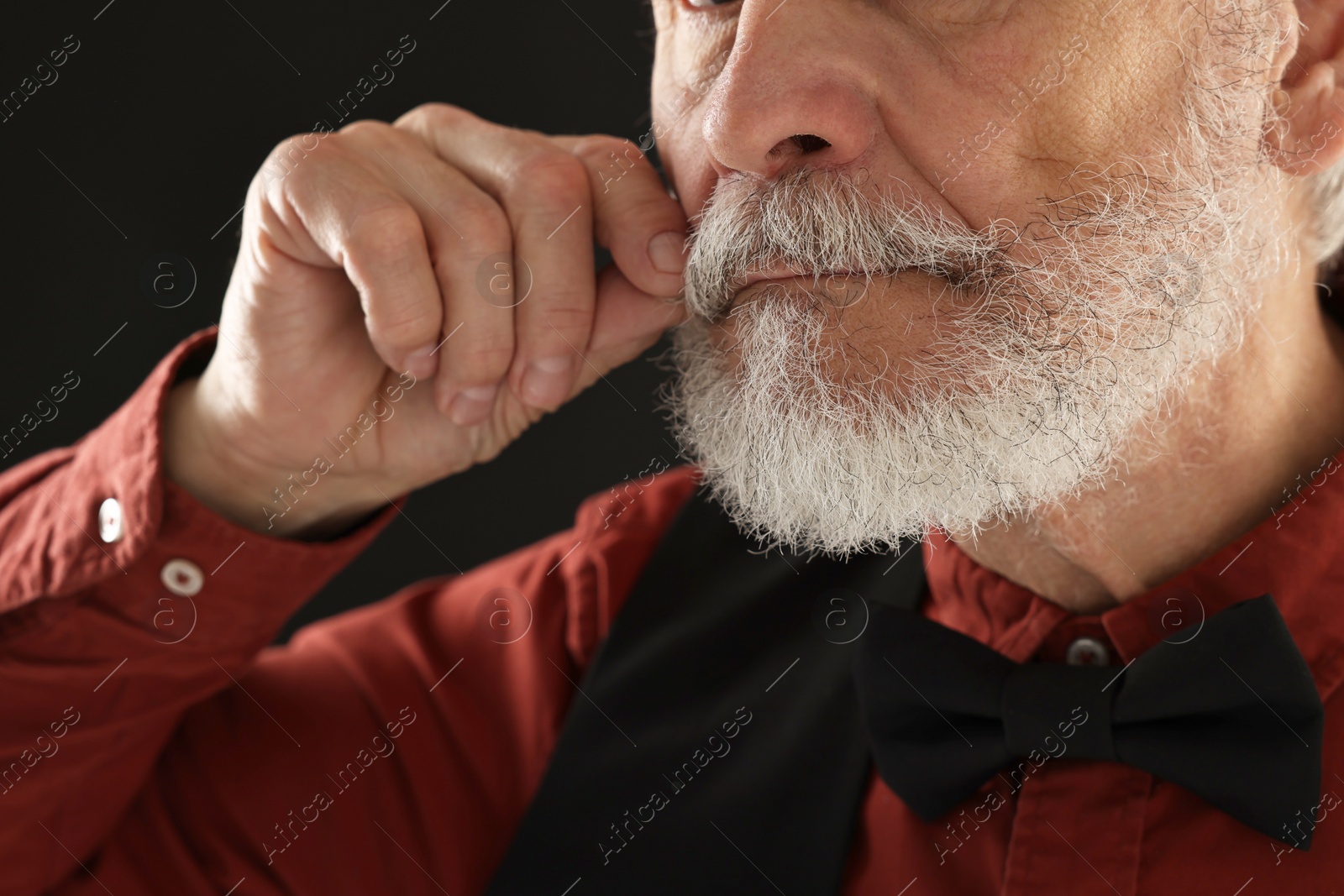 Photo of Man touching mustache on black background, closeup