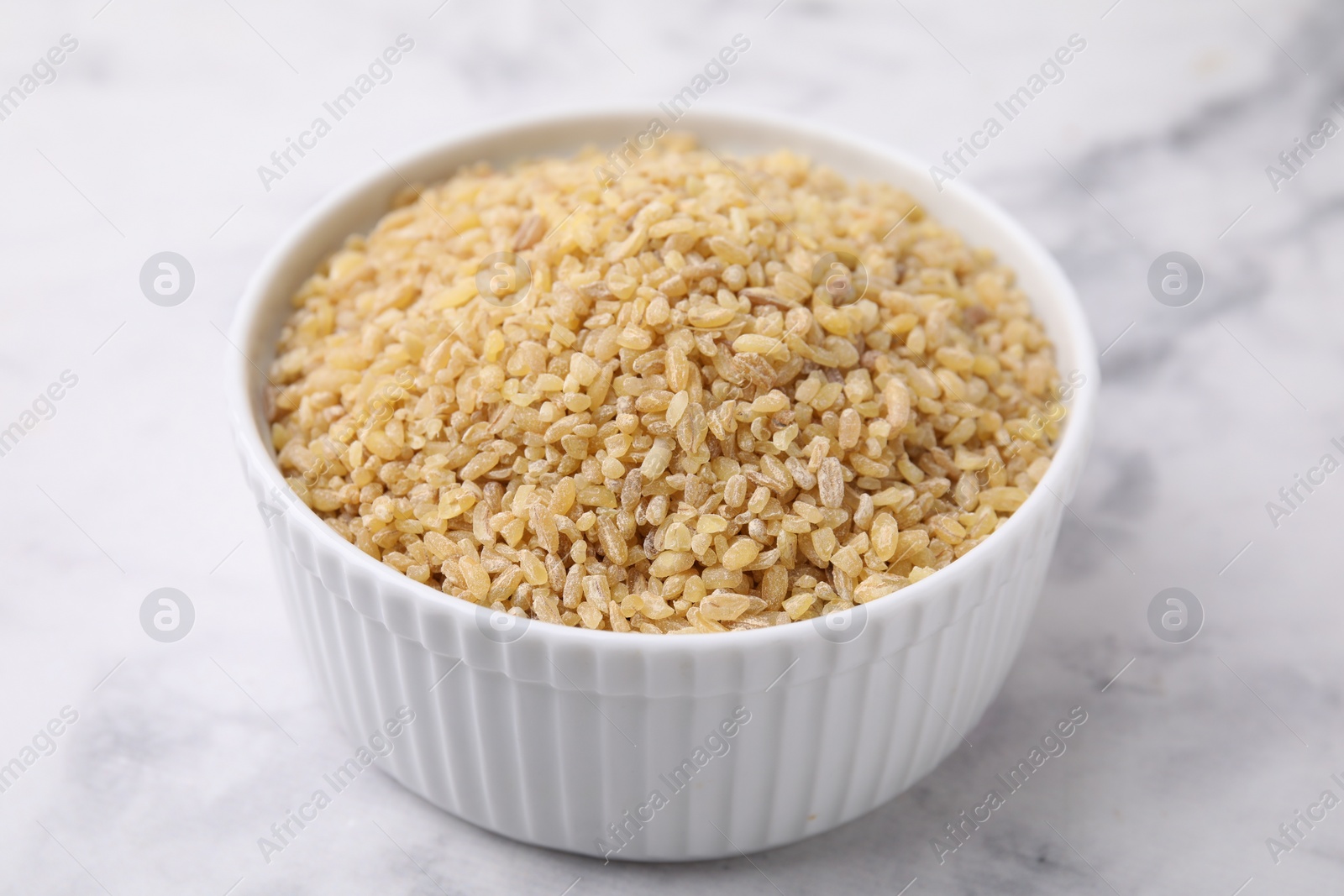 Photo of Raw bulgur in bowl on marble table, closeup