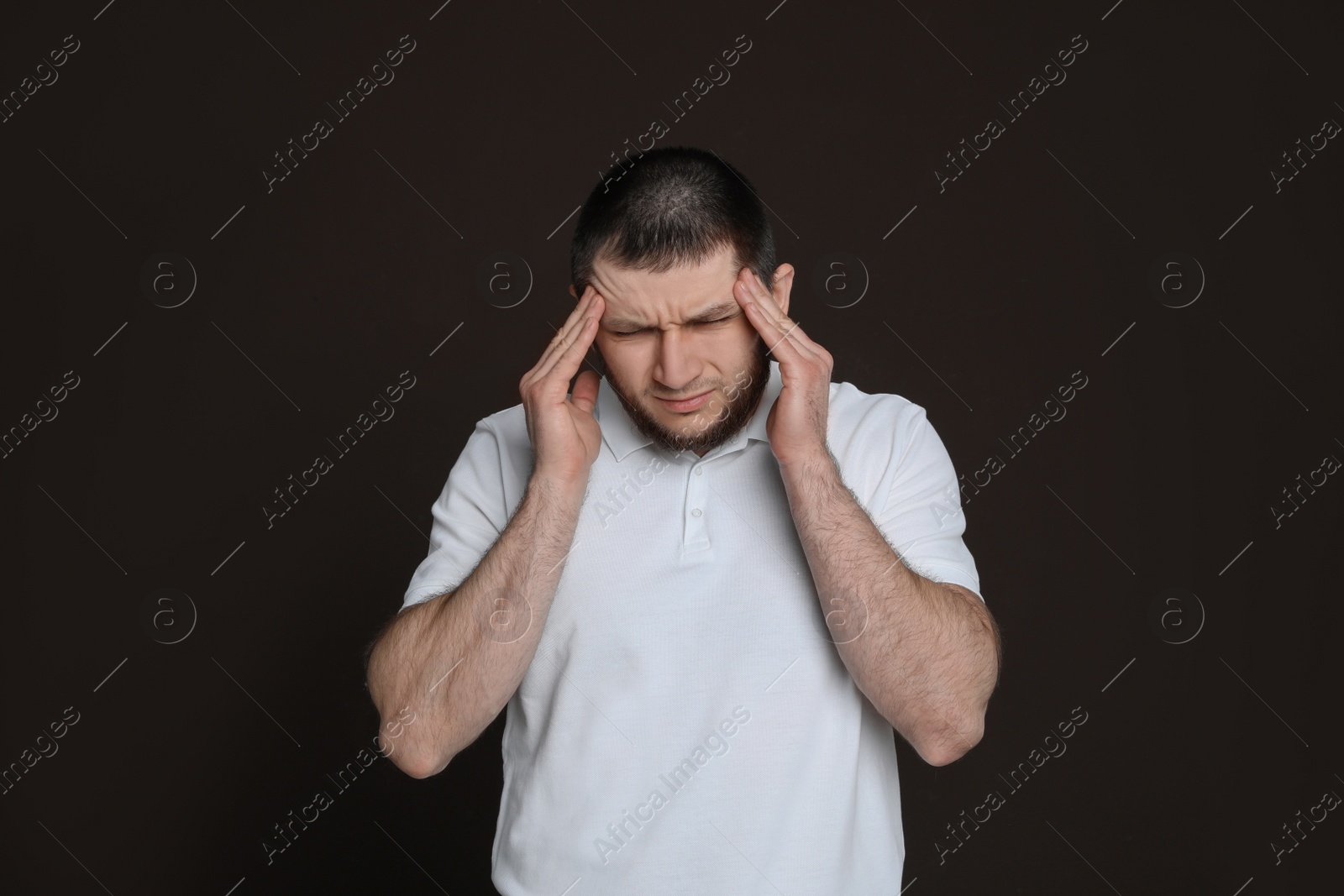 Photo of Man suffering from headache on dark brown background