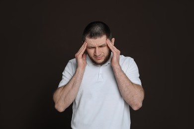 Man suffering from headache on dark brown background