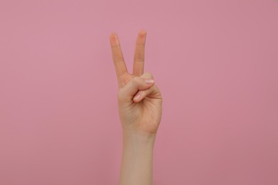 Photo of Woman showing two fingers on pink background, closeup