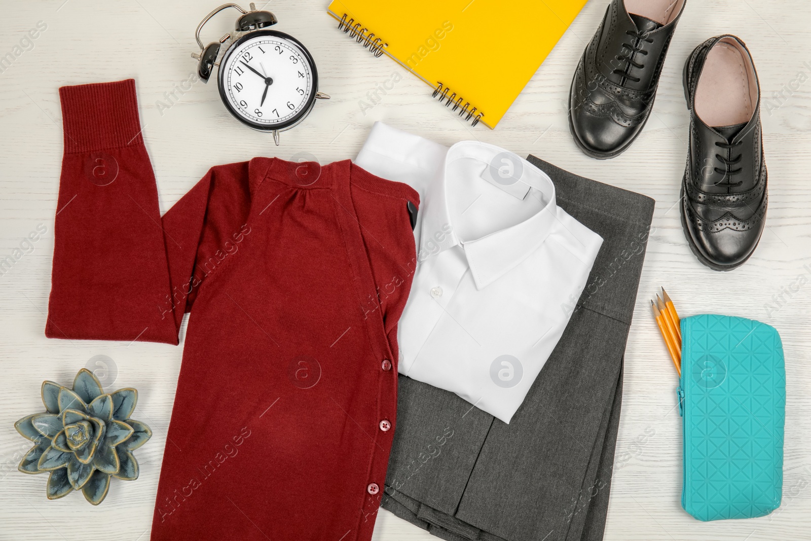 Photo of School uniform for girl and alarm clock on white wooden background, top view