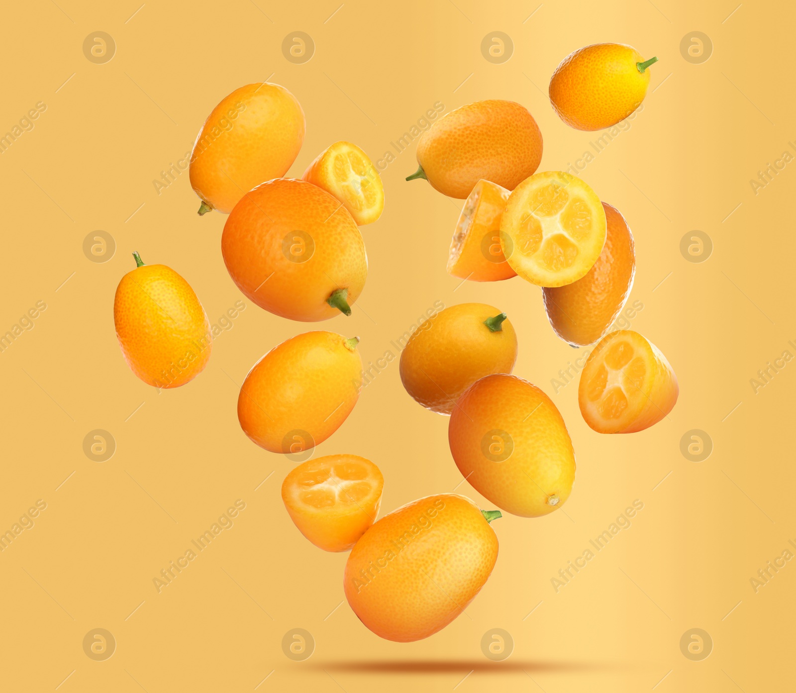 Image of Delicious whole and cut kumquats falling on pale orange background