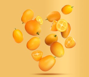 Delicious whole and cut kumquats falling on pale orange background