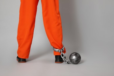 Prisoner in orange jumpsuit with metal ball on grey background, closeup. Space for text
